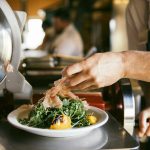 Chef preparing a fresh salad with greens and tomatoes in a professional kitchen.