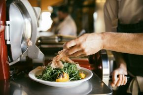 Chef preparing a fresh salad with greens and tomatoes in a professional kitchen.