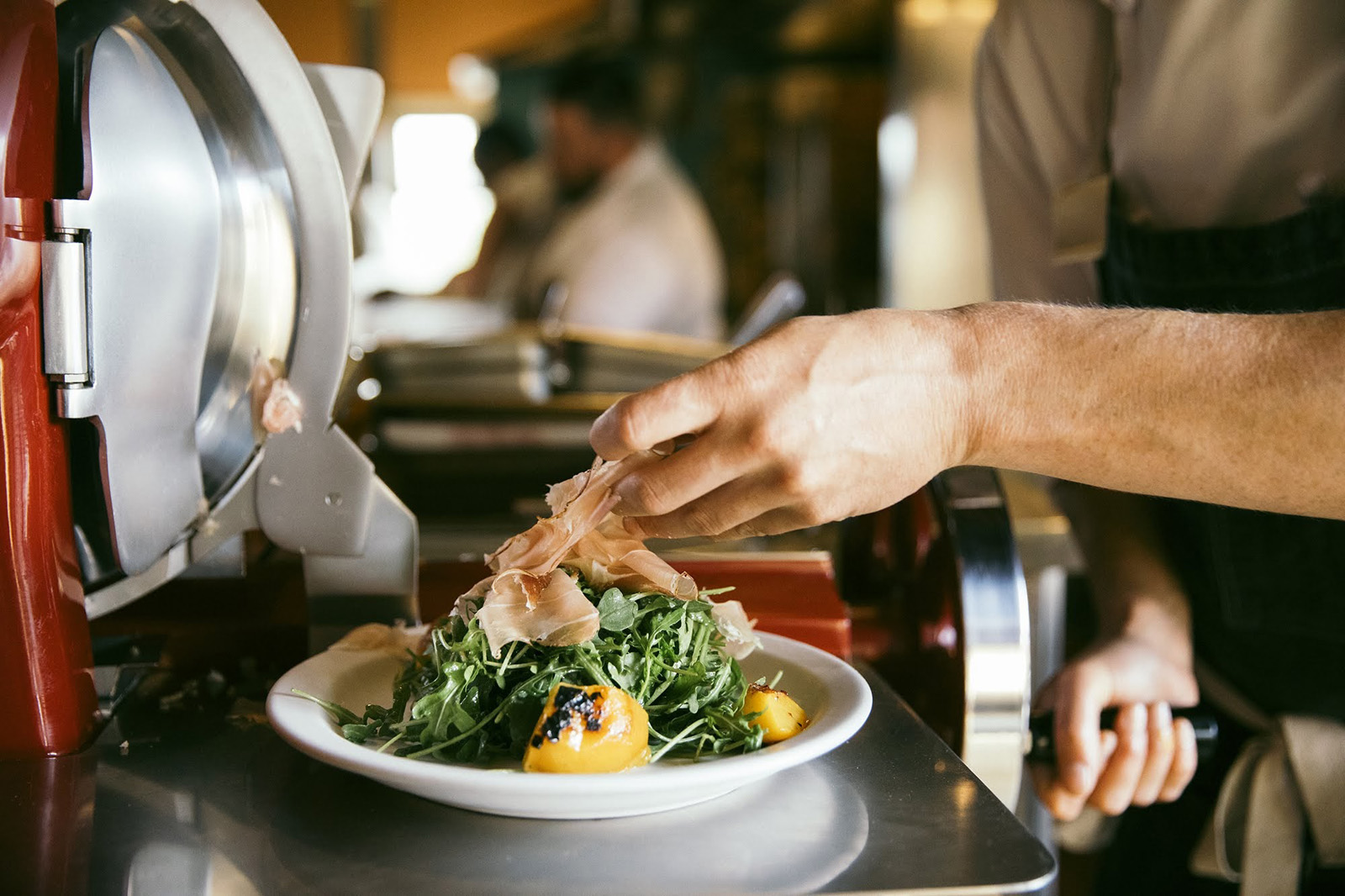 Chef preparing a fresh salad with greens and tomatoes in a professional kitchen.