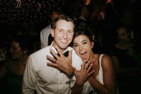 Bride and groom laughing and showing their wedding rings during a lively reception.