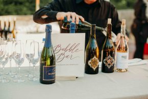 Bartender pouring wine at a wedding bar with bottles and a ‘Bubbly Bar’ sign on display