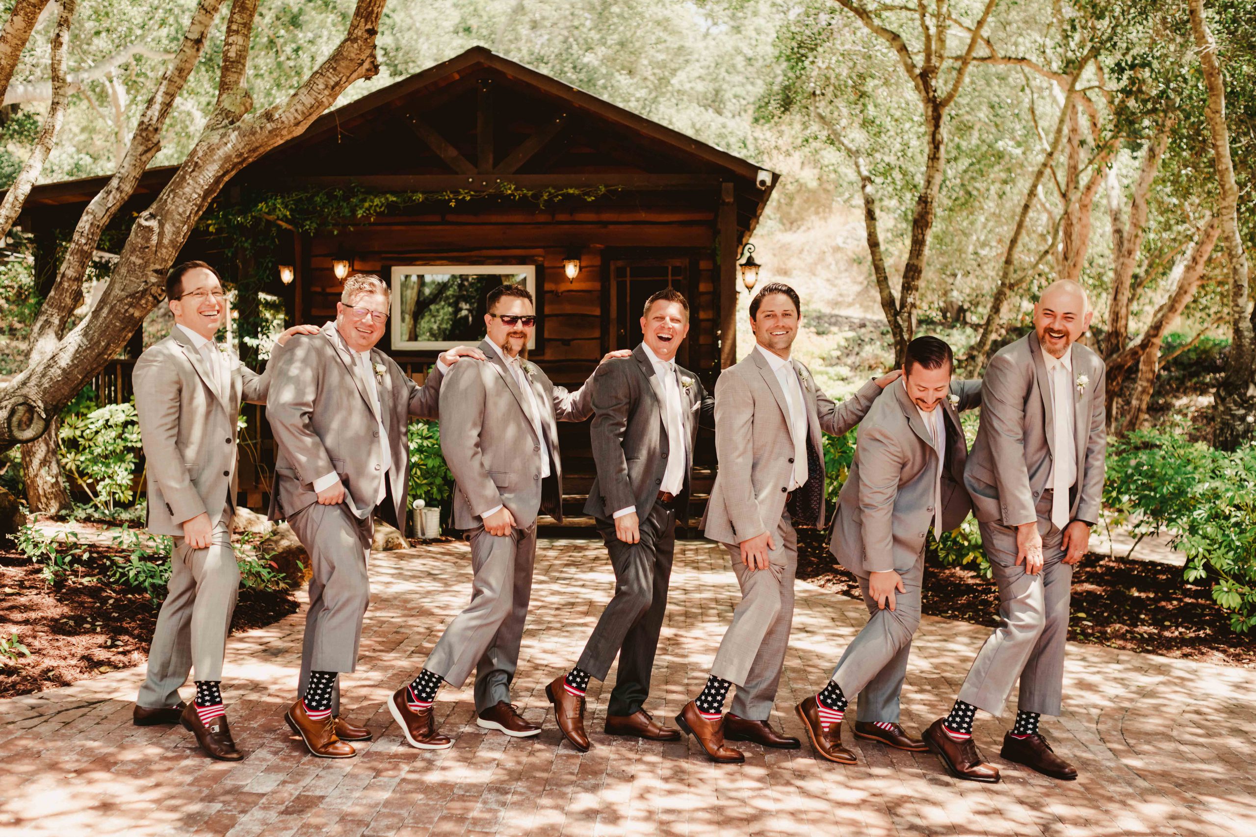 Groomsmen in light gray suits posing playfully in a wooded