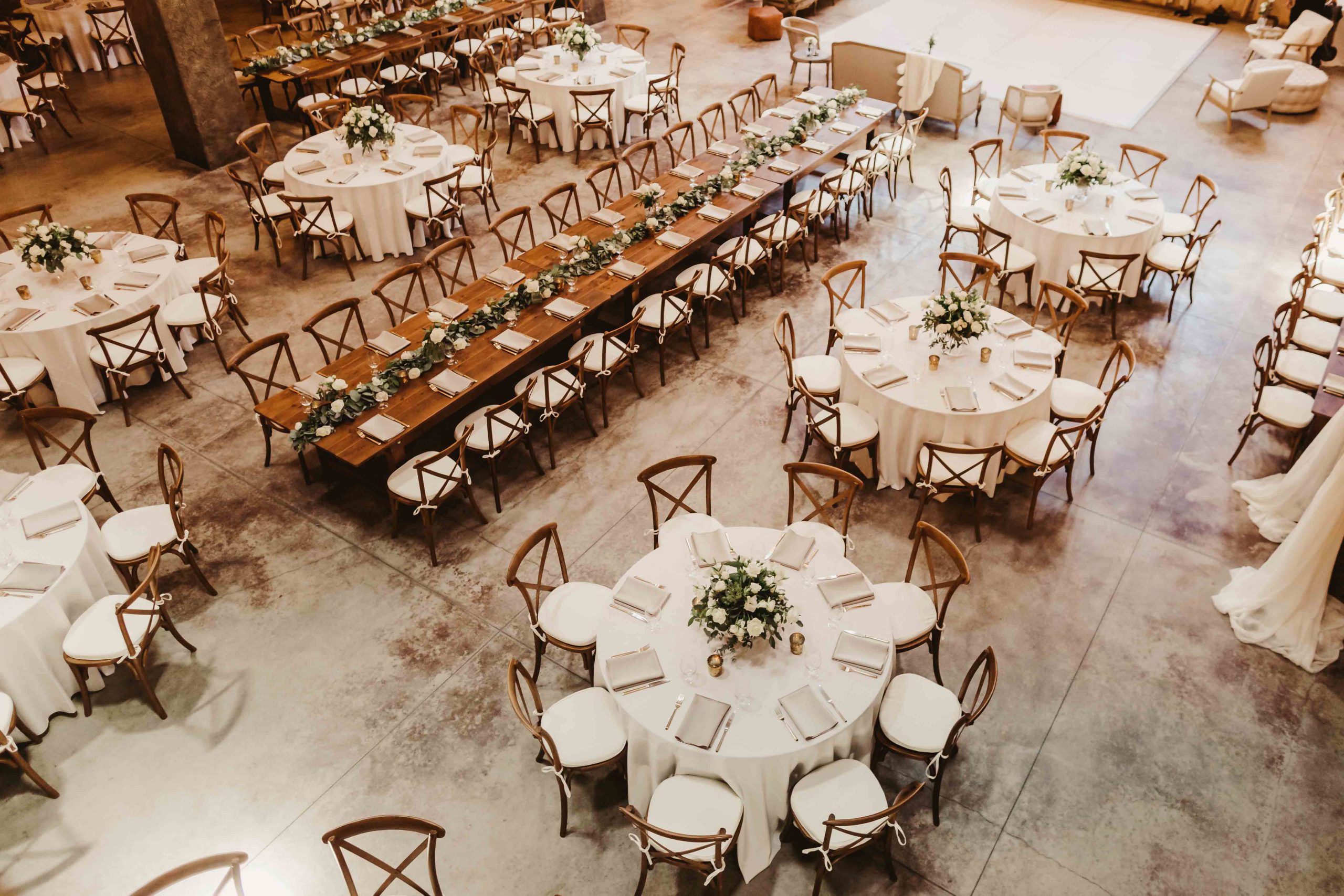 Rustic indoor venue arranged with mixed table styles, white linens, and simple floral décor.